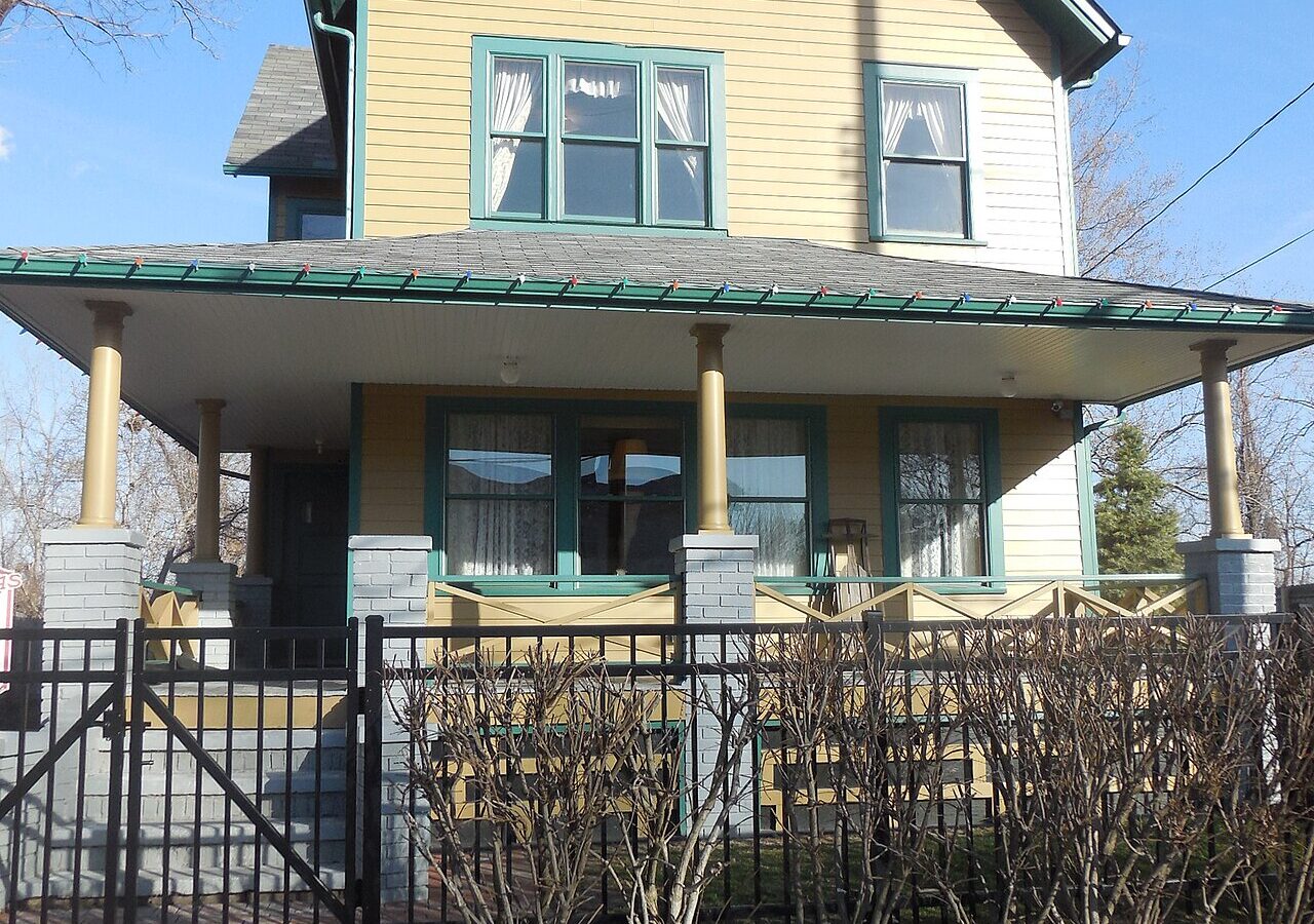 Yellow two-story house with green trim and a wide front porch behind a black iron fence in Cleveland, Ohio